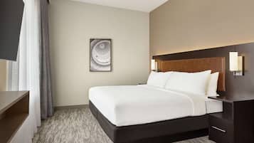 A hotel room with a large bed, a wooden headboard, bedside lamps, a flat-screen TV, and a framed artwork on the wall.
