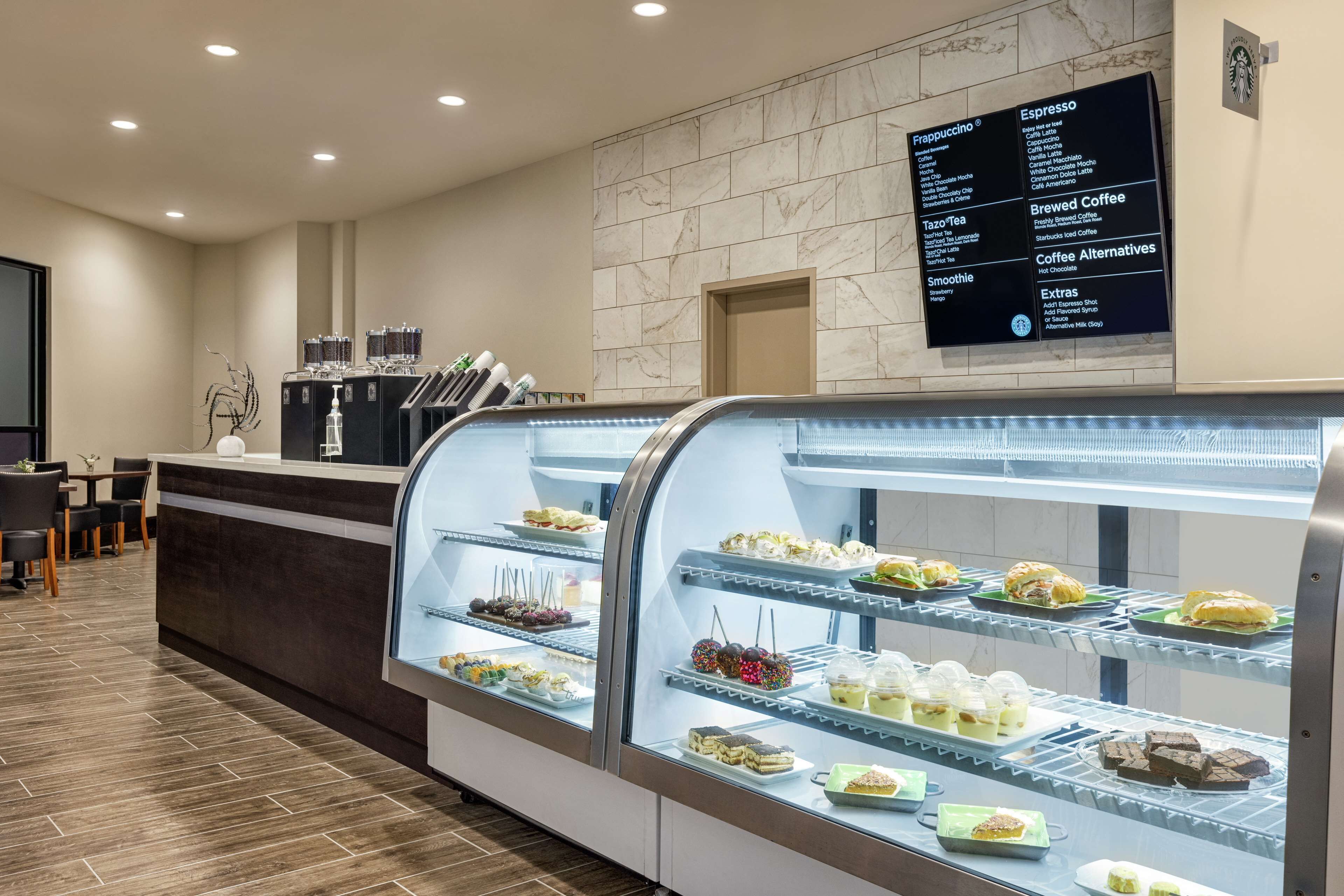 Un vestíbulo de hotel con una estación de café, un panel de menú y una presentación de postres.