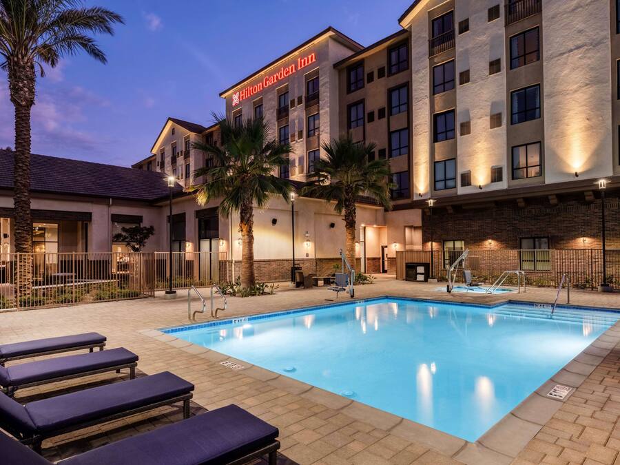 Een Hilton Garden Inn met een zwembad, lounge stoelen en palmbomen.