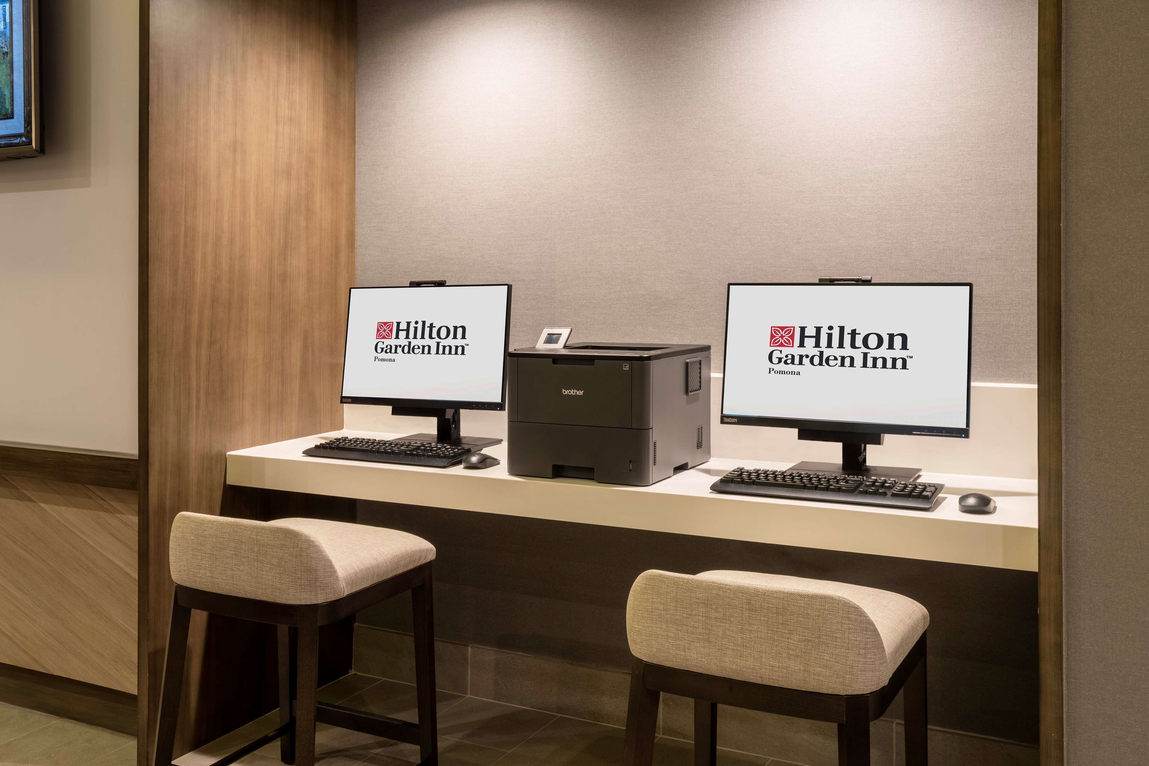 En reception på Hilton Garden Inn med to computorskærme, en printer og to polstrede barstole.