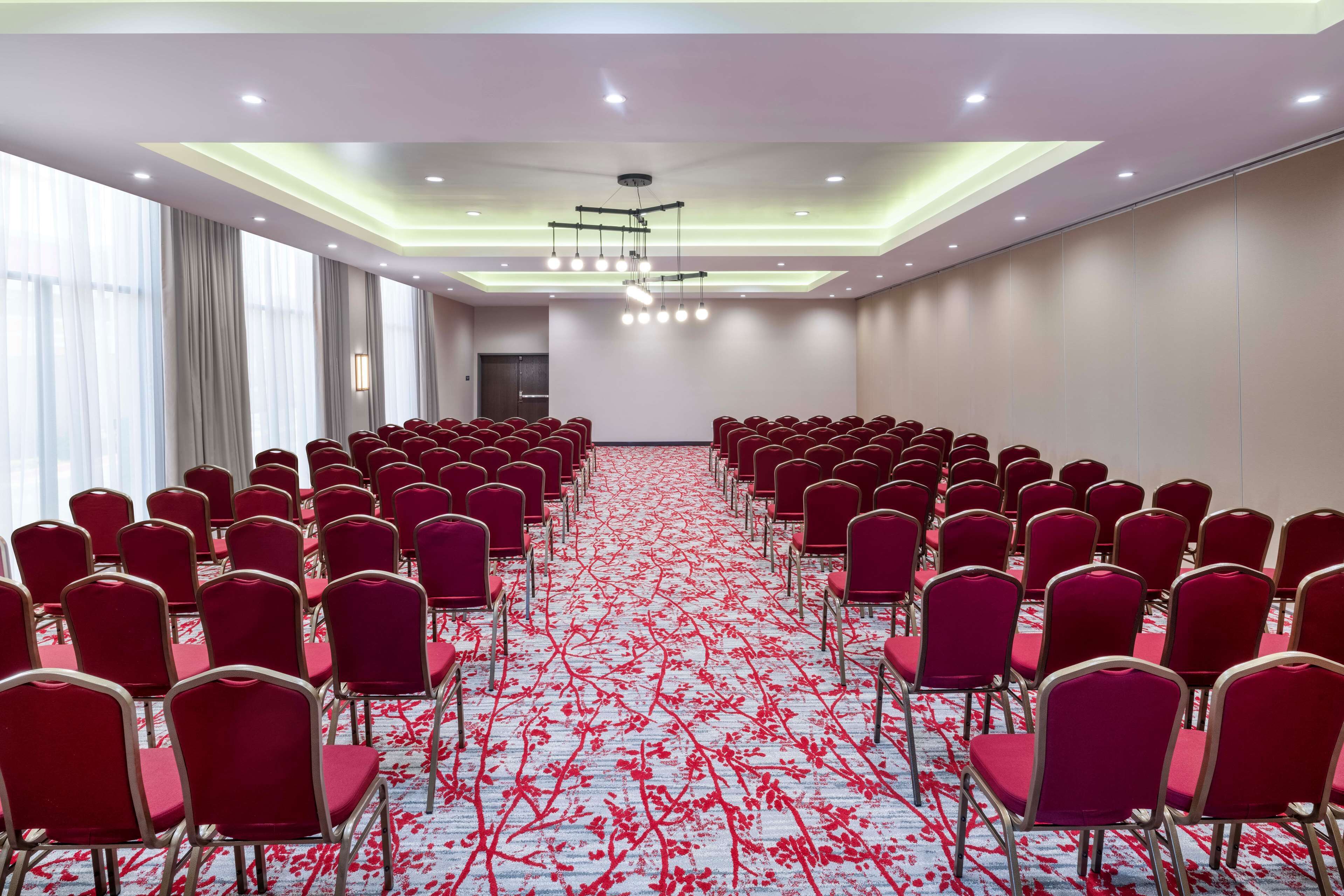 A conference room with rows of red chairs and a carpet with a red floral pattern.