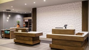 Un espace d’accueil d’hôtel avec un comptoir de réception en bois, un mini-bar, une plante et un réfrigérateur à vin.