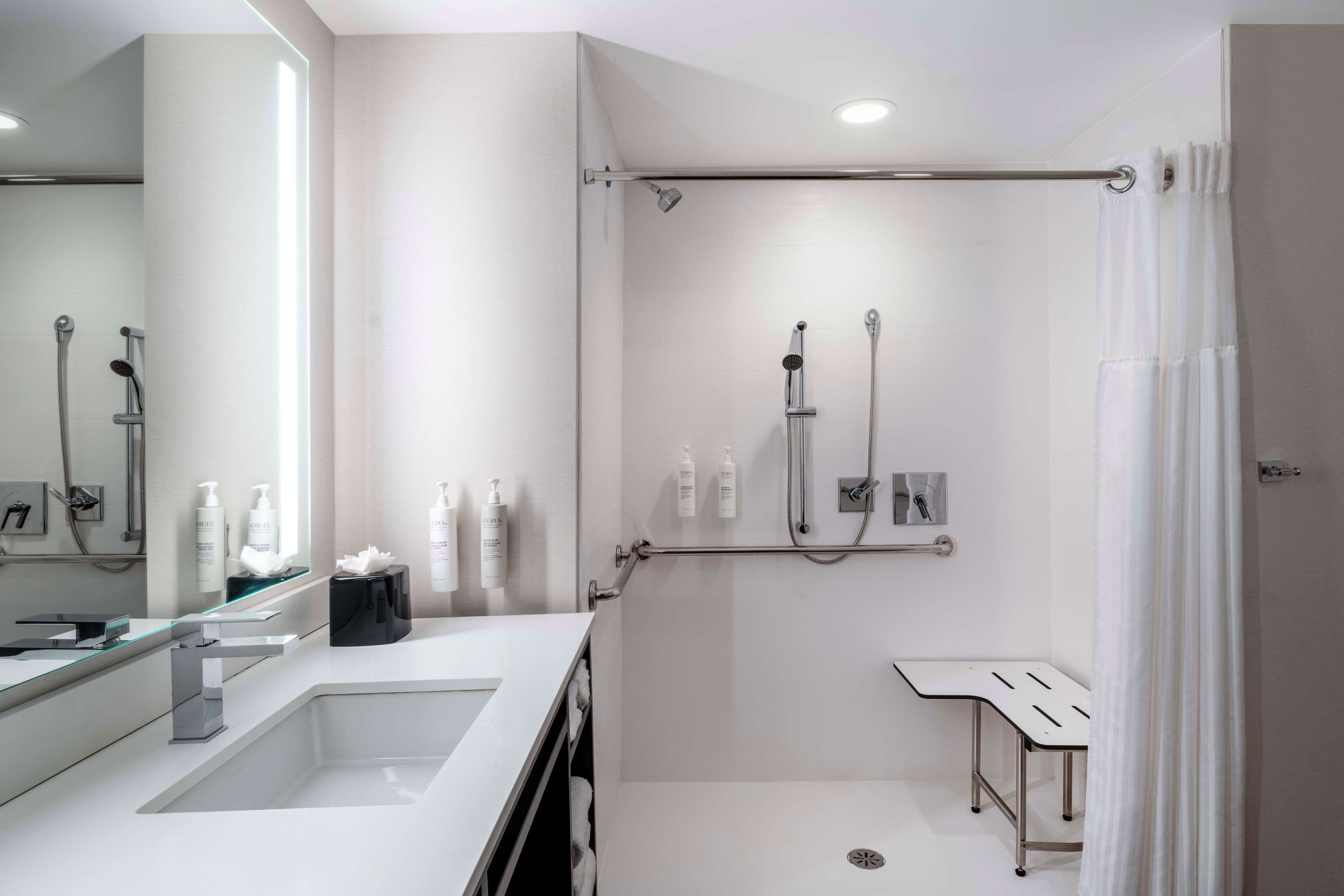 Une salle de bain moderne avec une douche à l’italienne en verre, un meuble-lavabo doté d’un grand miroir et un lavabo blanc.