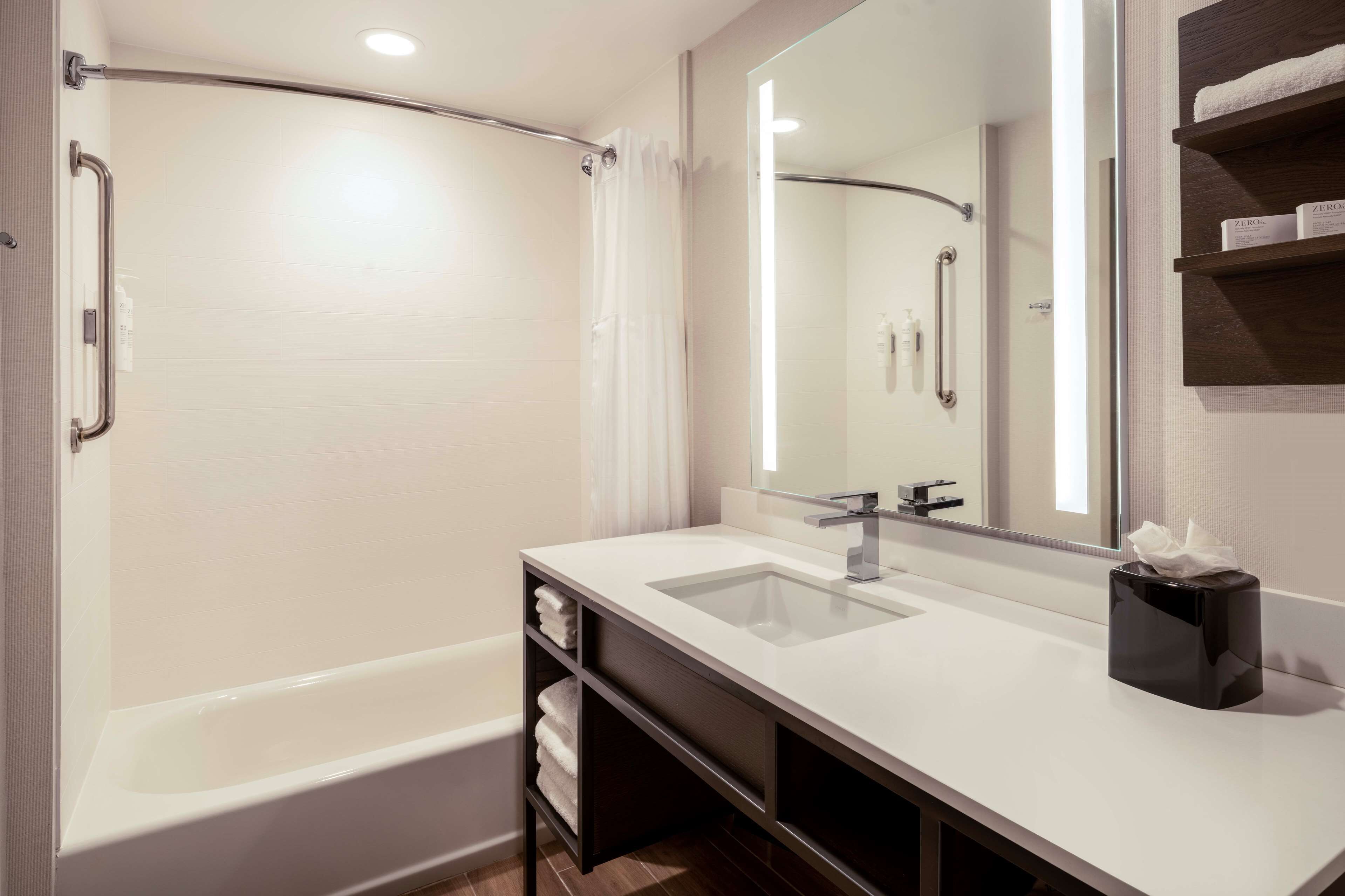 Un baño moderno con bañera, un espejo grande, lavamanos y un perchero para toallas.