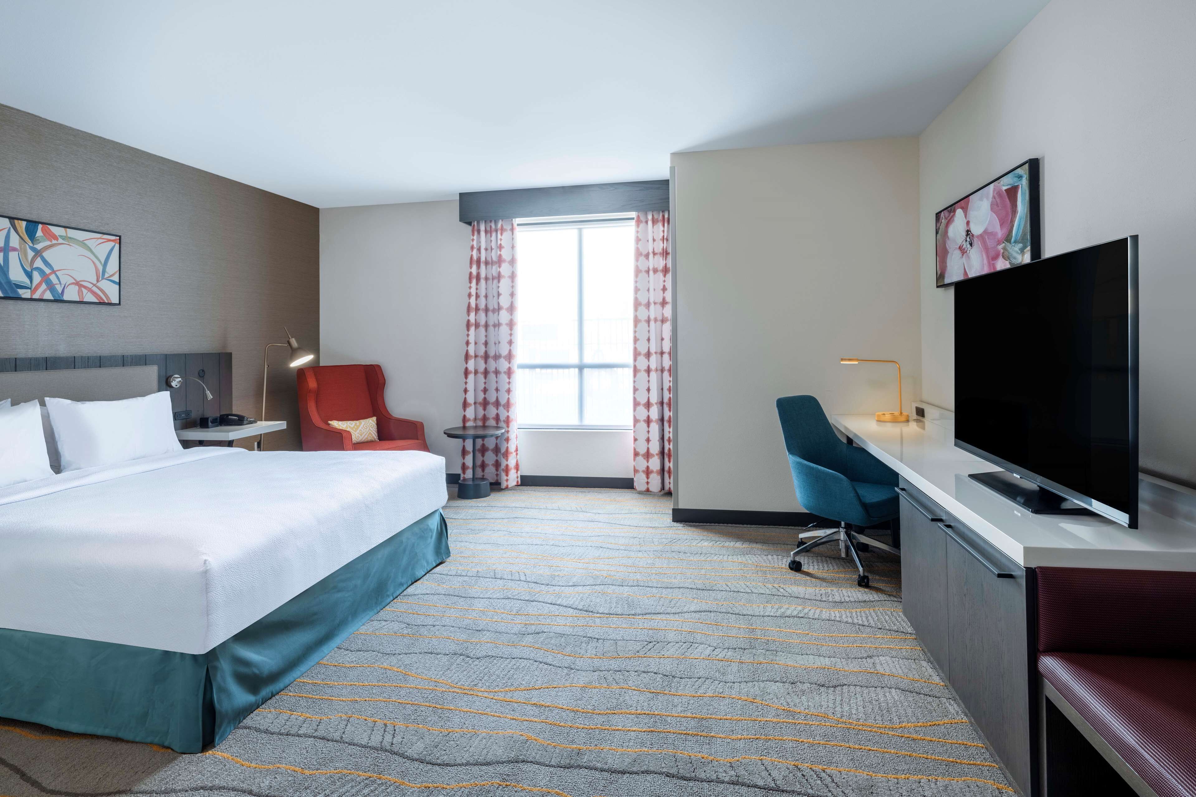A hotel room with a bed, a desk, a TV, a chair, a desk lamp, and a window with curtains.