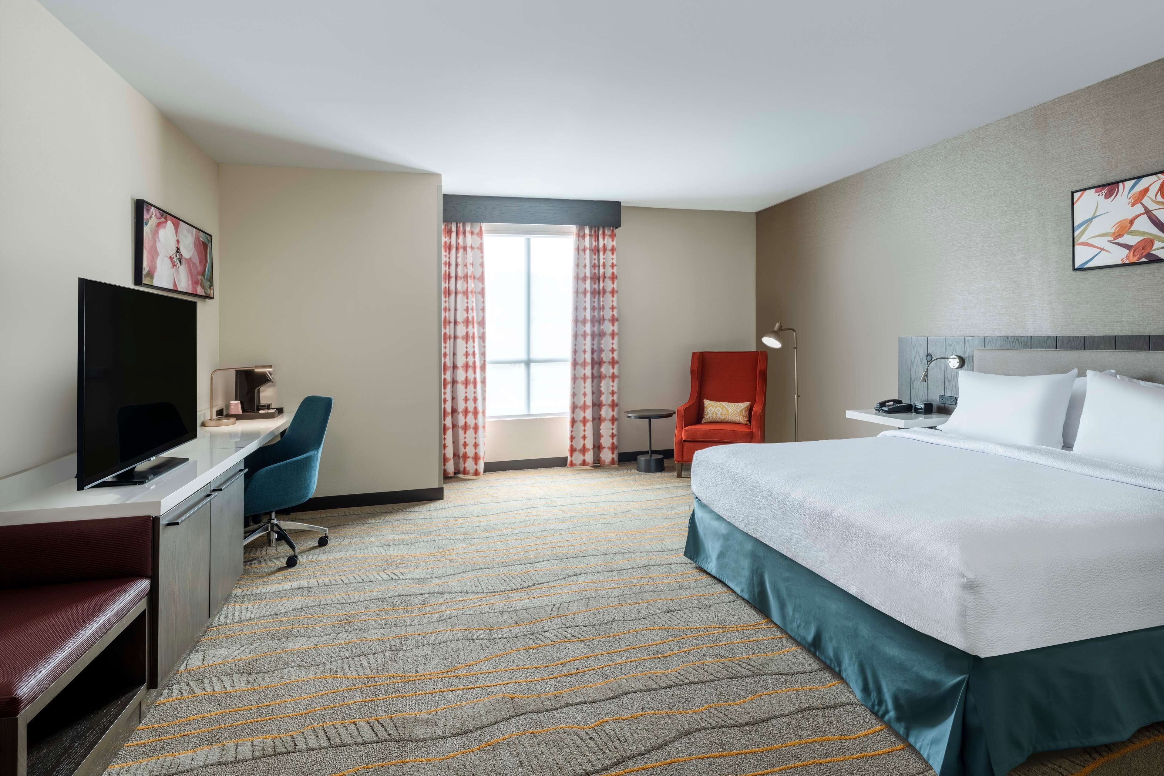 A hotel room with a bed, desk, chair, television, and a window with curtains.