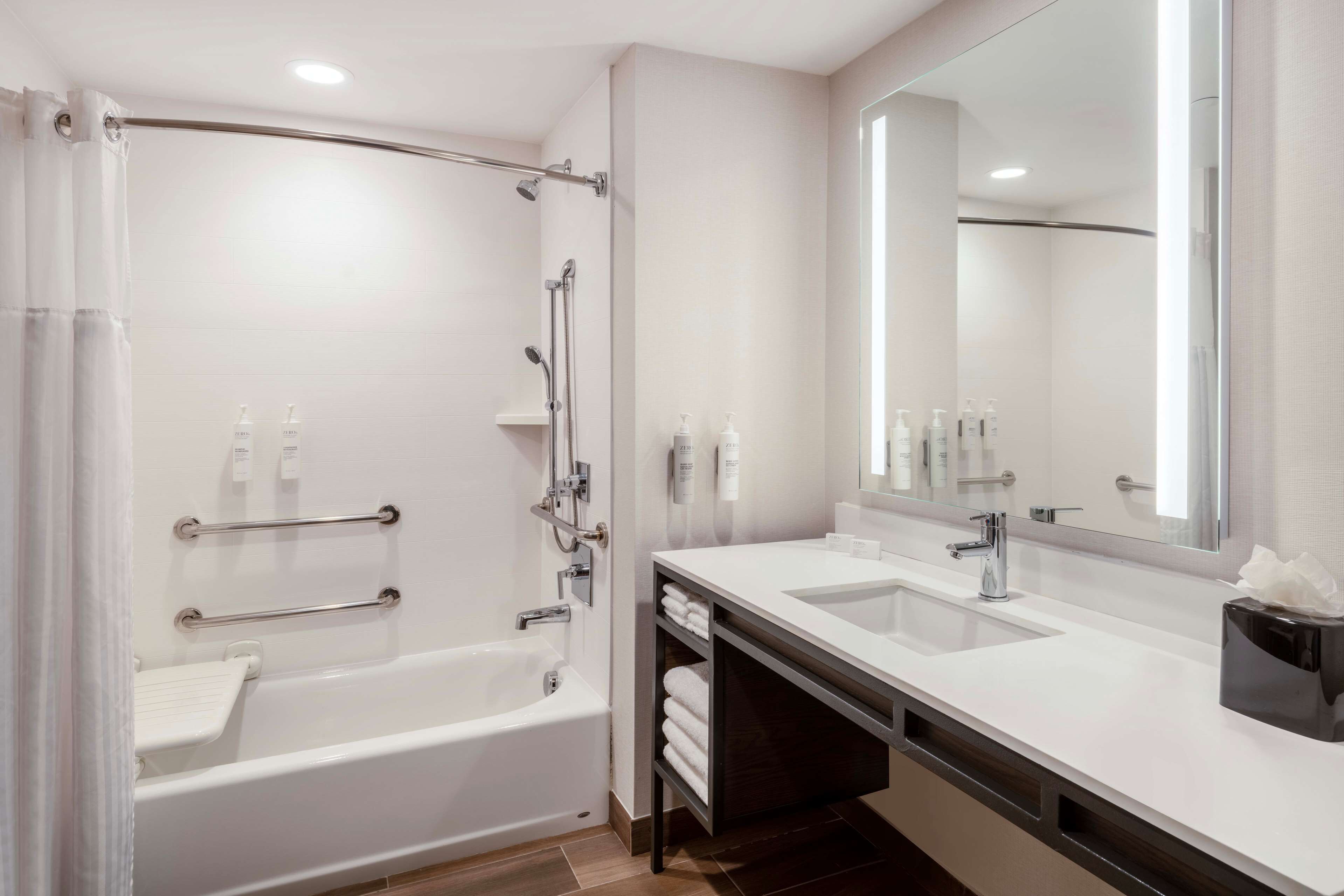A modern bathroom with a bathtub, two sinks, a large mirror, and handrails.