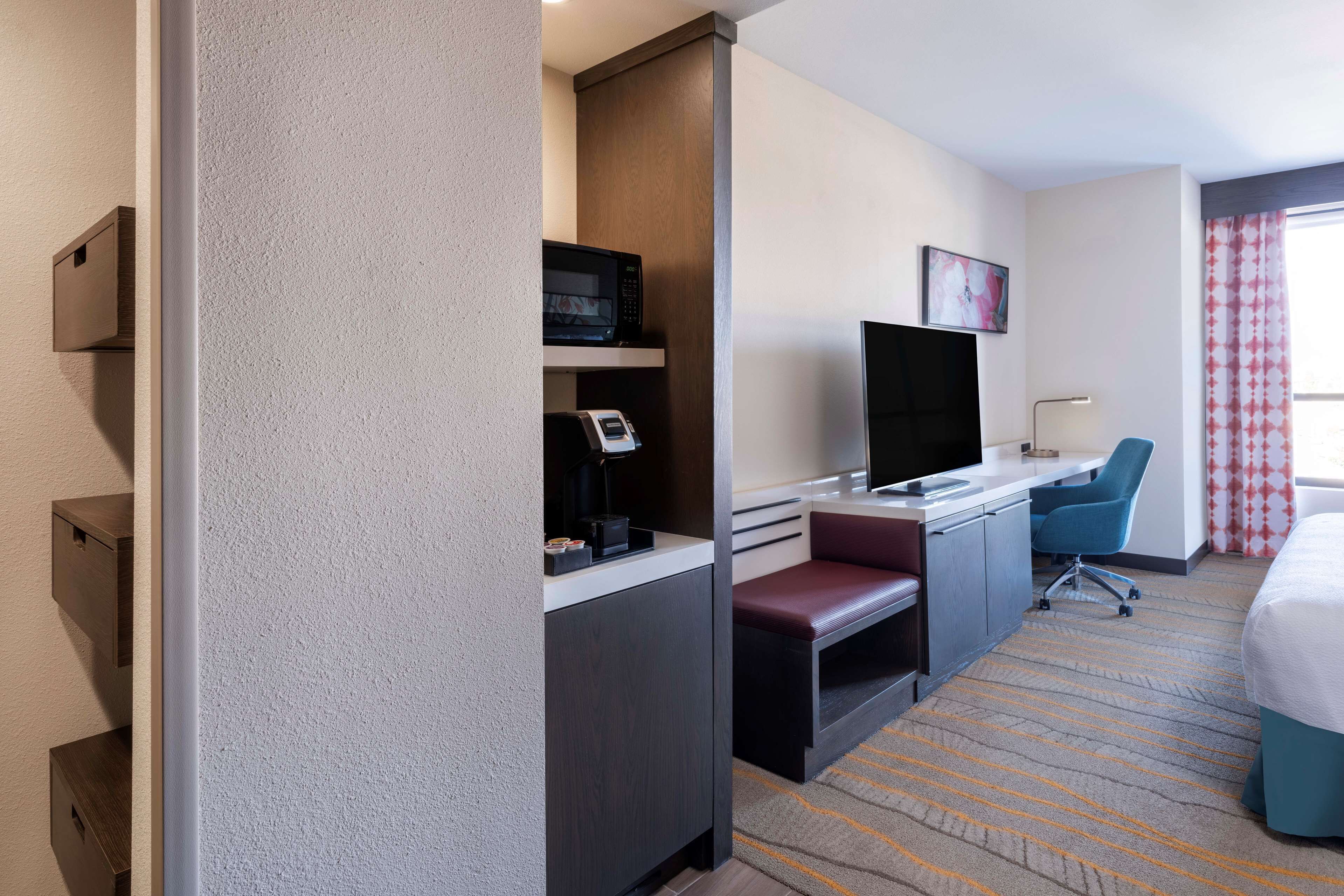 Una habitación de hotel con escritorio, televisor, silla, cama y ventana con cortinas.