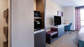 Una habitación de hotel con escritorio, televisor, silla, cama y ventana con cortinas.