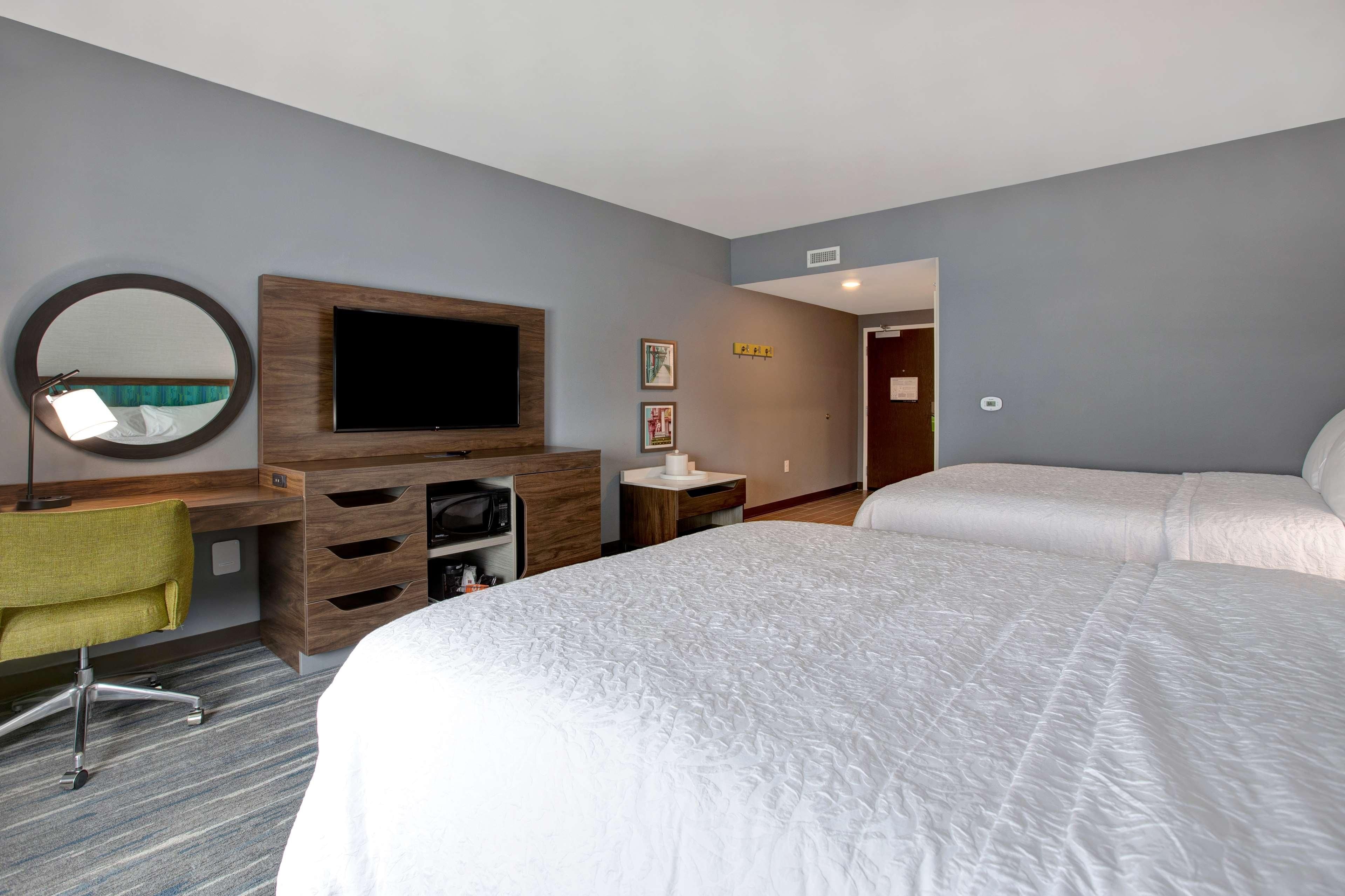A hotel room with a large bed, a desk with a chair, a TV, and a mirror.
