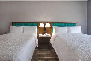 A hotel room with two beds, a small bedside table with a lamp, and a wooden headboard.