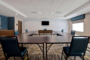 Uma sala de conferência com uma mesa comprida, cadeiras, uma TV de tela plana e uma janela.