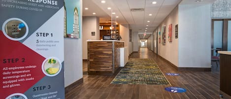 A hotel reception area with a 3-step response poster, a reception desk, and a hallway leading to guest rooms.