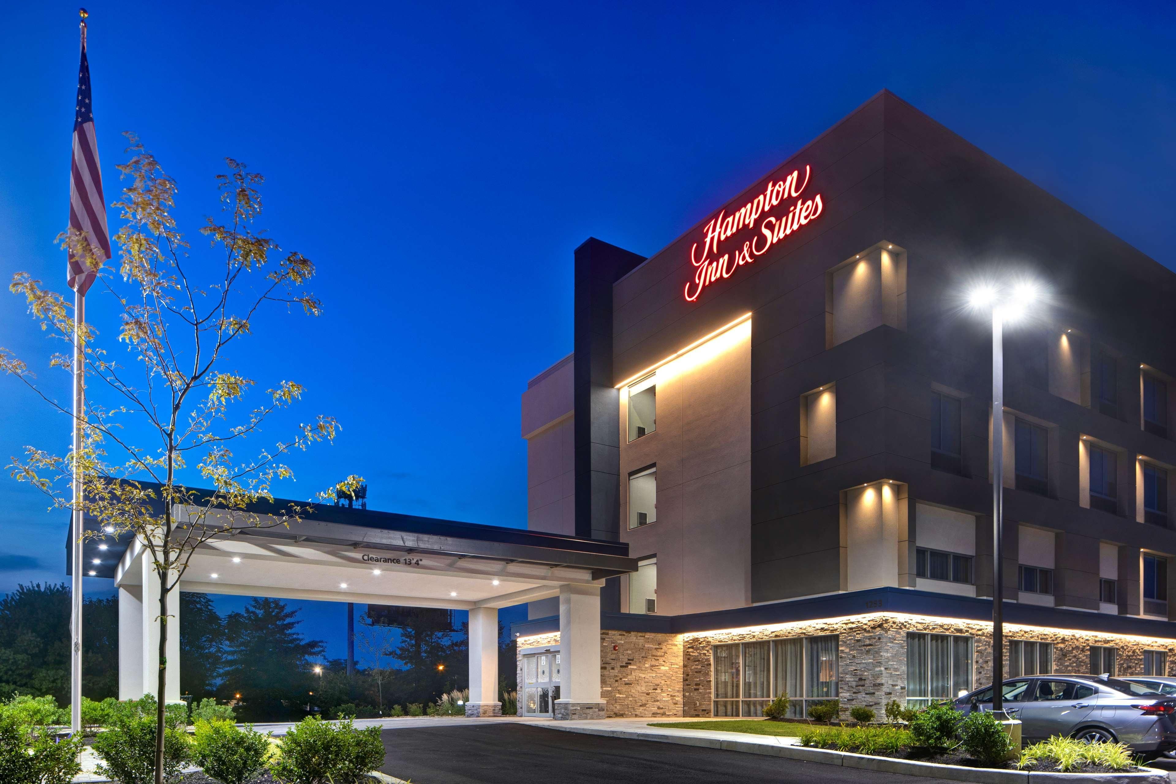 Een Hampton Inn & Suites hotel met een heldere lucht, een Amerikaanse vlag en een goed verlichte ingang.