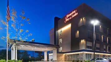 A Hampton Inn & Suites hotel with a clear sky, an American flag, and a well-lit entrance.
