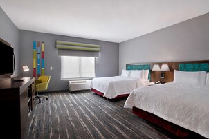 A hotel room with two beds, a desk, a chair, a TV, and a window with blinds.
