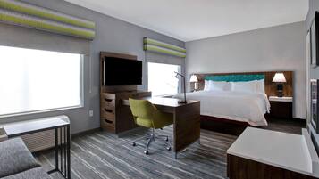 A hotel room with a bed, desk, chair, television, and a window with blinds.