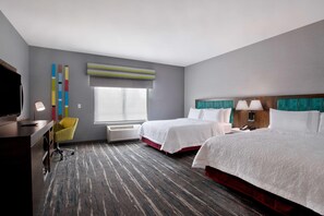 Quarto de hotel com duas camas, uma escrivaninha, uma cadeira, uma televisão e uma janela com persianas.
