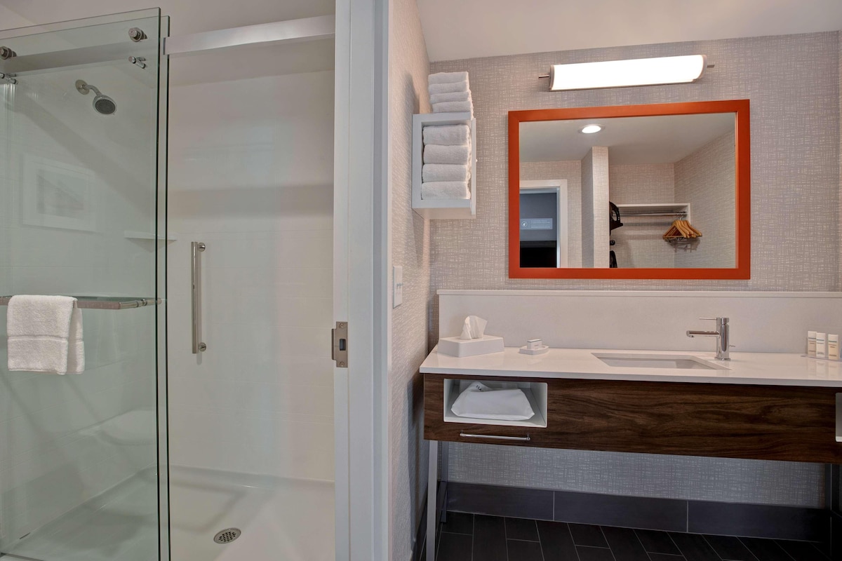 A modern bathroom with a glass shower enclosure, a white sink with a wooden vanity, and a large mirror with an orange frame.