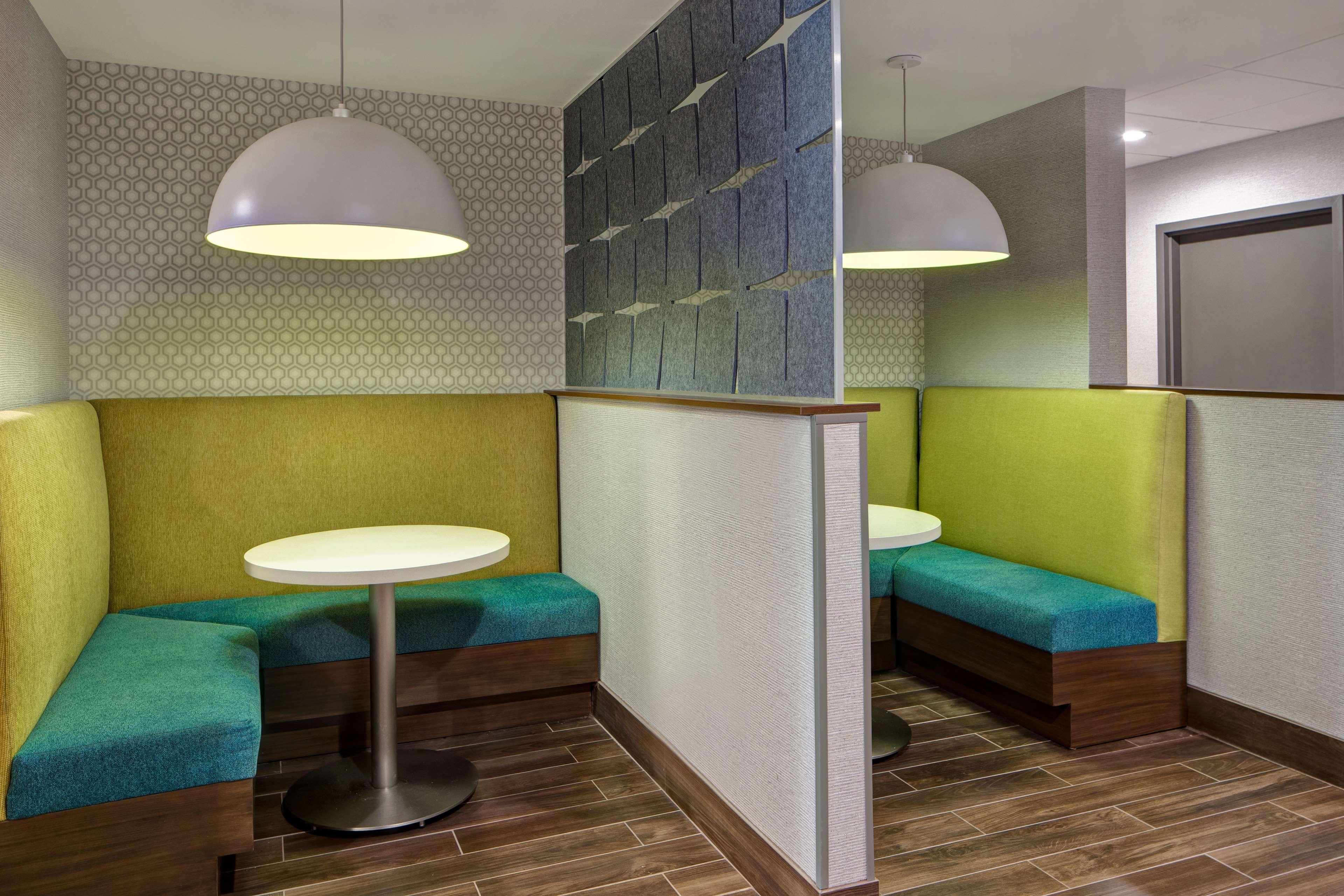 Un interior moderno con una zona de estar que incluye bancos acolchados y mesas redondas, un papel tapiz con diseño e iluminación colgante.