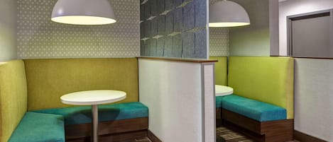 A modern interior with a seating area featuring cushioned benches and round tables, a patterned wall, and pendant lighting.