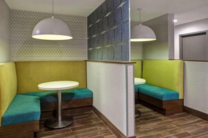 Un interior moderno con una zona de estar que incluye bancos acolchados y mesas redondas, un papel tapiz con diseño e iluminación colgante.