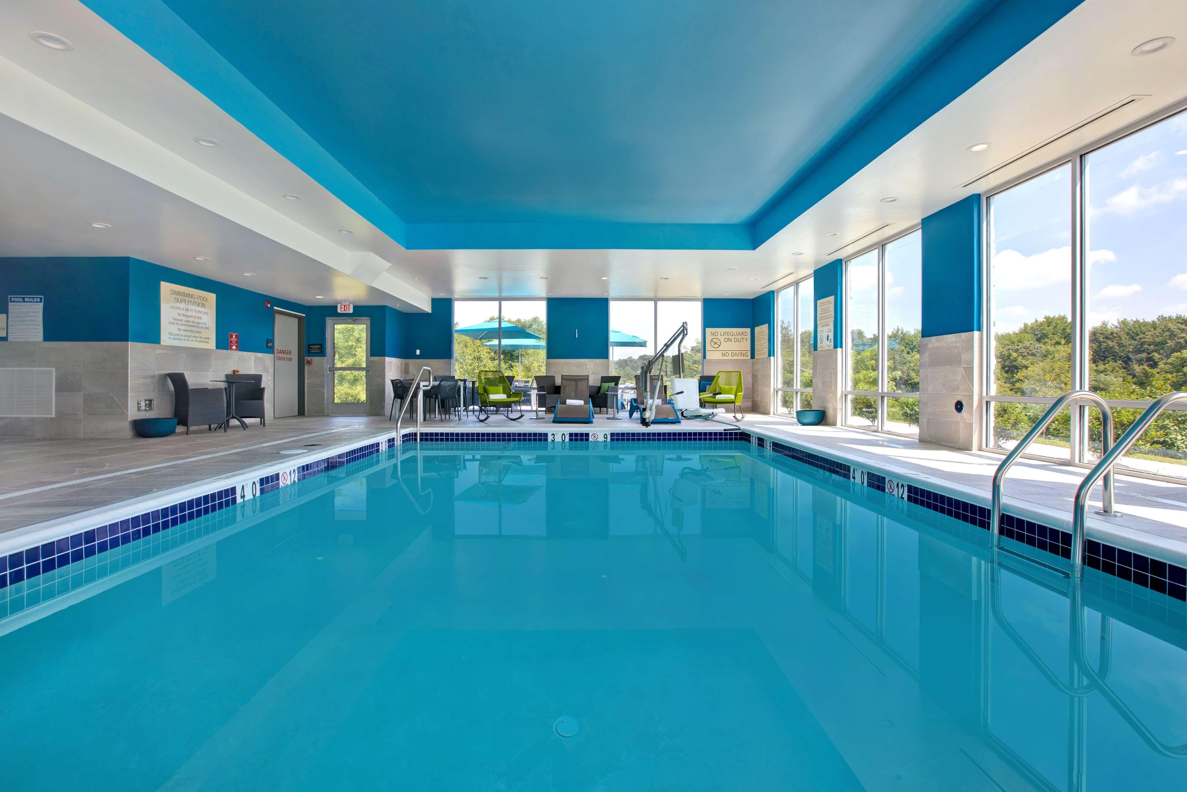 Una piscina interior moderna con agua cristalina azul, tragaluces y vistas a los árboles circundantes.