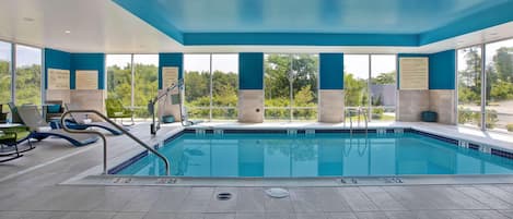 An indoor swimming pool with clear safety signage, a lifeguard chair, and a view of the outdoors.