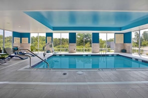 Una piscina interior con señalización de seguridad clara, una silla de socorrista y vistas al exterior.