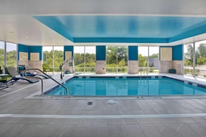 Una piscina interior con zonas de piscina despejadas, señales de seguridad y vistas a la vegetación circundante.