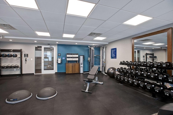 A gym with exercise equipment, a bench, and a wall-mounted mirror. - Hampton Inn And Suites Deptford (Woodbury)