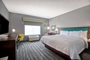 Una habitación de hotel con una cama grande, un escritorio con silla, televisor y ventana con persianas.