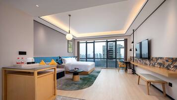 A modern hotel room with a bed, desk, and seating area.