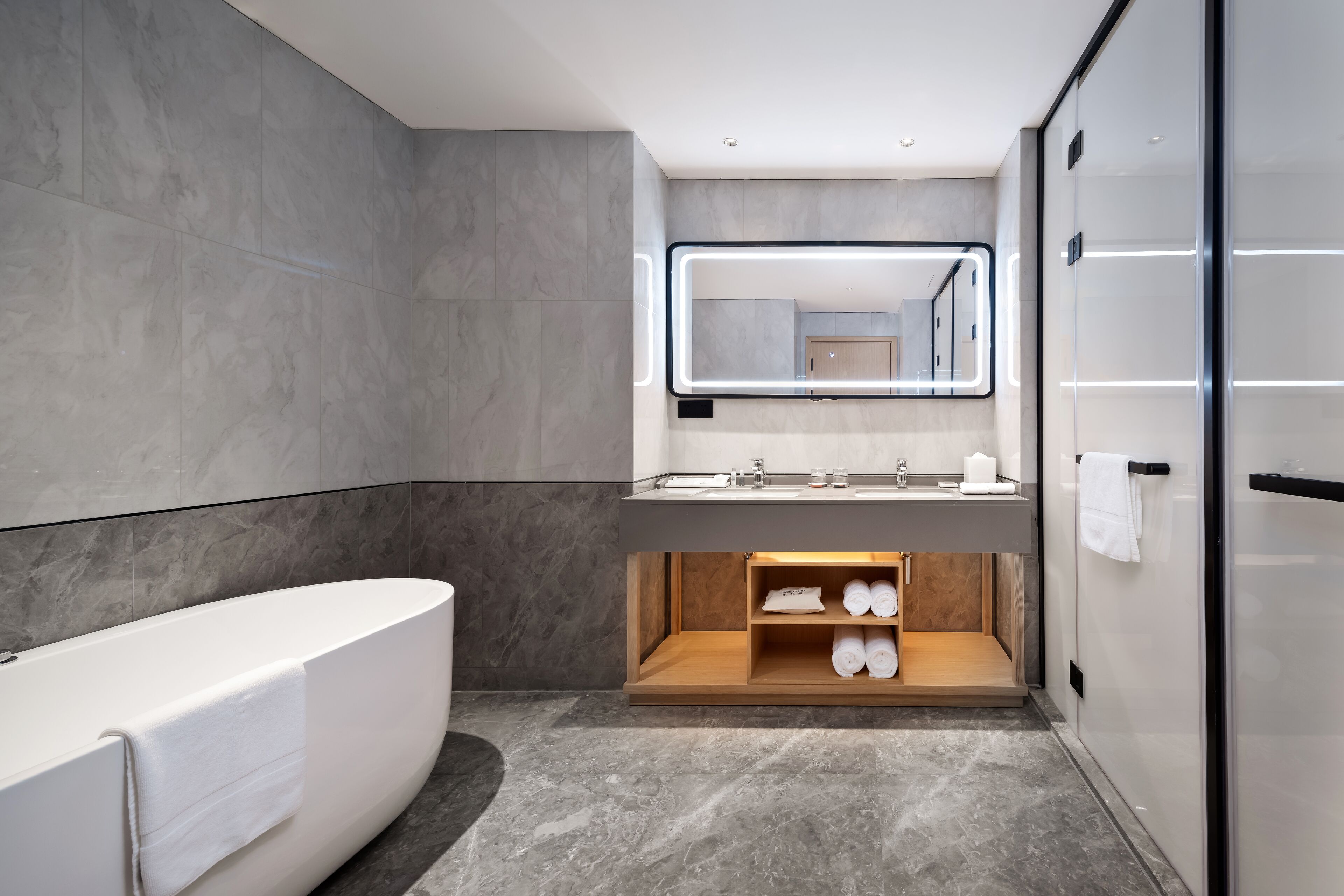 A modern bathroom with a large bathtub, a vanity with a mirror, and a wooden shelf under the sink.