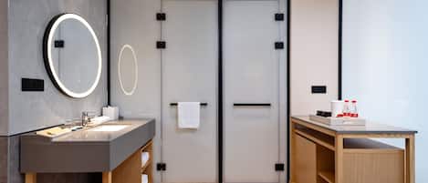 A modern bathroom with a grey vanity, a round mirror, a towel rack, and a wooden cabinet.