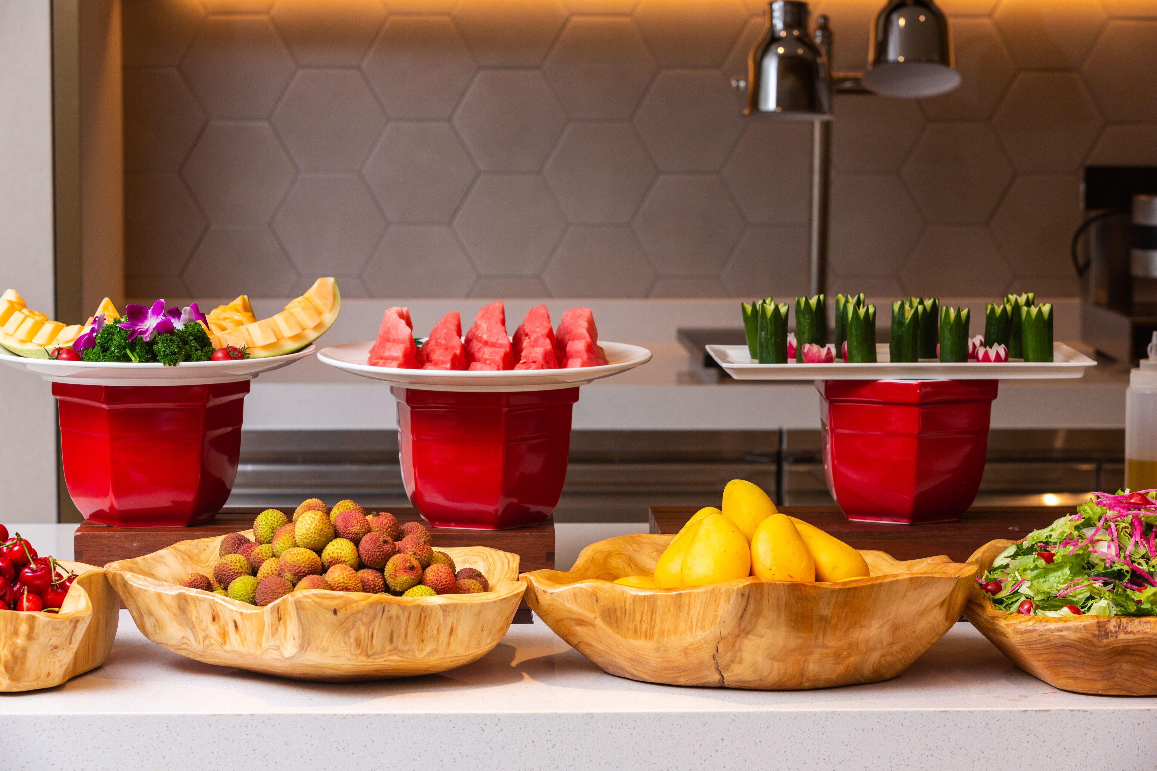 Ein Buffet mit einer Auswahl an Früchten und Gemüsen, darunter Wassermelone, Litschis und grünen Zwiebeln, präsentiert in roten und hölzernen Schalen.