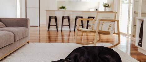 Een woonkamer met een zwarte hond die op een vloerkleed ligt, een bank en een eethoek met stoelen en een tafel.
