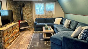 Ein Wohnzimmer mit einem Ecksofa, einer Holzkistenkommode, einem Fernseher und einem Deckenventilator.