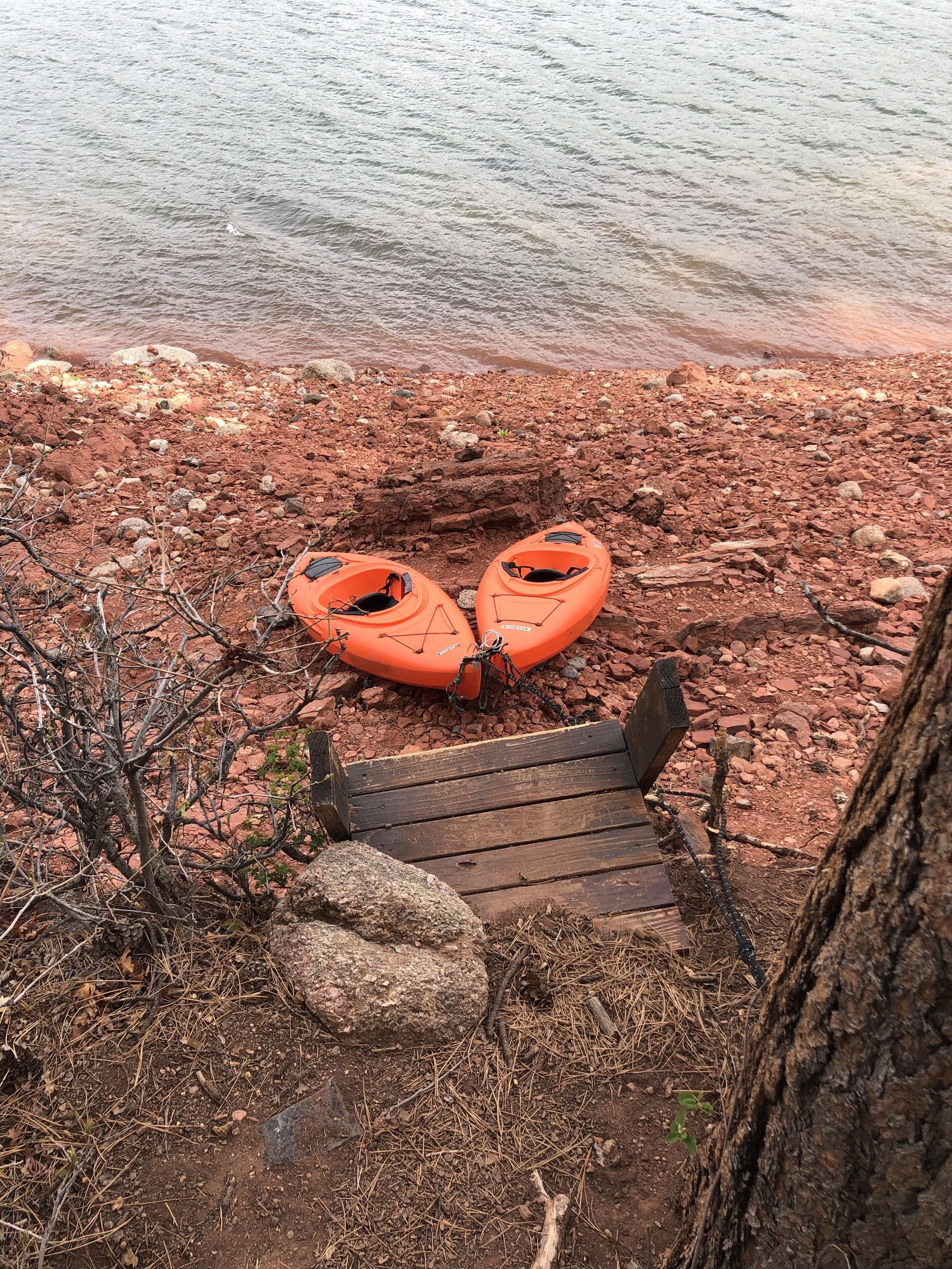 Two orange kayaks on a rocky shore with a wooden dock leading to the water.