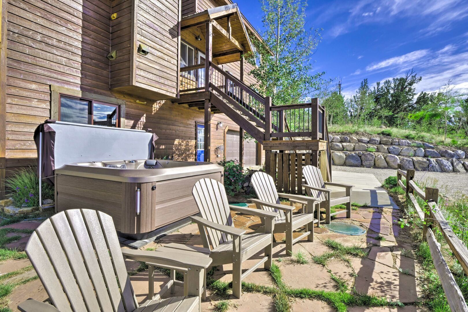 A wooden cabin with a hot tub, outdoor seating, and a stone retaining wall.