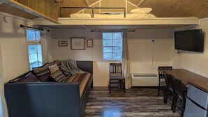 A compact room with a bunk bed, a sofa, a dining table, and a TV. - Tiny Rock House (Franklin)