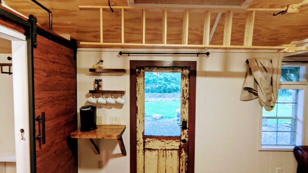 A rustic kitchen with wooden beams, a coffee maker, and a view of the outdoors through a door. - Tiny Rock House (Franklin)