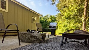 A patio area with a stone table, a grill, and a cat on a rock. - Tiny Rock House (Franklin)