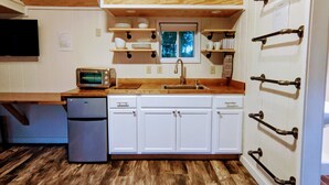 A compact kitchen with white cabinets, a wooden countertop, a built-in oven, a microwave, and a window above the sink. - Tiny Rock House (Franklin)
