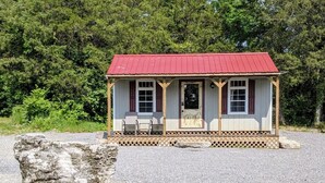 A small cabin with a red roof, wooden porch, and a gravel driveway. - Tiny Rock House (Franklin)