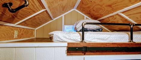 A dormitory room with a bunk bed, wooden ceiling, and a white door with a towel rack.