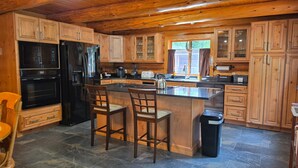 Une cuisine avec des meubles de rangement en bois, un réfrigérateur noir, une cuisinière, un évier et une fenêtre.
