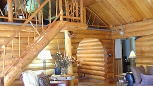 L’intérieur d’une cabane en rondins, avec un escalier en bois, des meubles en cuir et une décoration rustique.