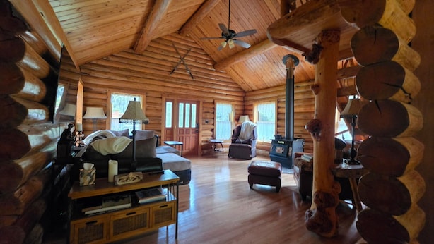 L’intérieur d’une cabane en rondins, avec une cheminée, des meubles en bois et un ventilateur de plafond.