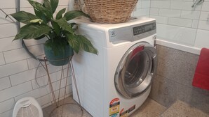Un lave-linge à chargement frontal, avec un panier placé sur le dessus, une plante en pot et une serviette rouge accrochée au mur.